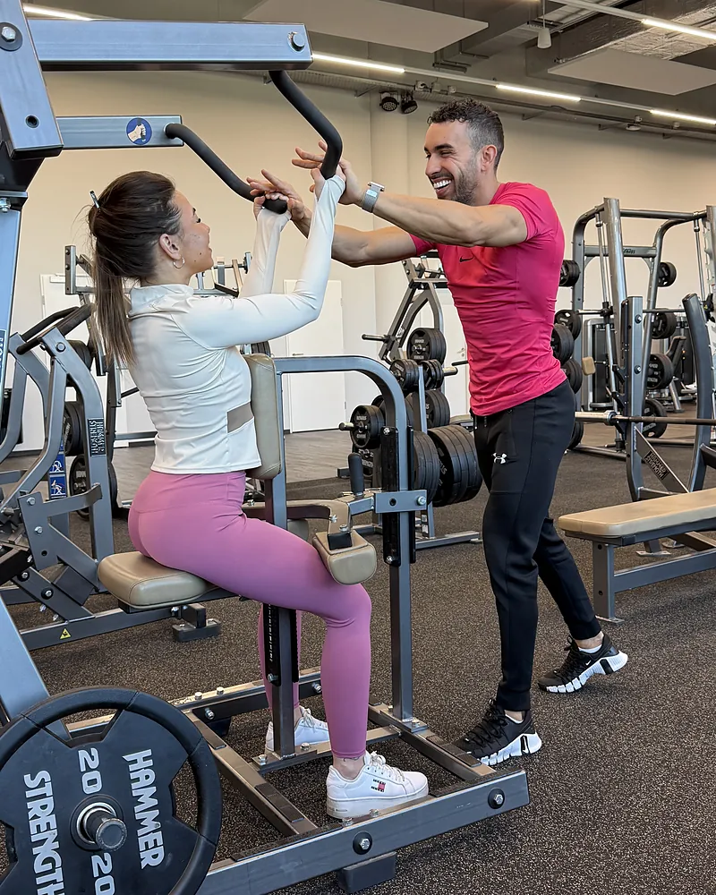 Samy guide une cliente sur une machine de musculation Hammer Strength